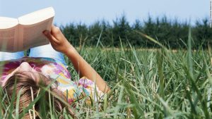 girl lying on grass reading book, relaxing